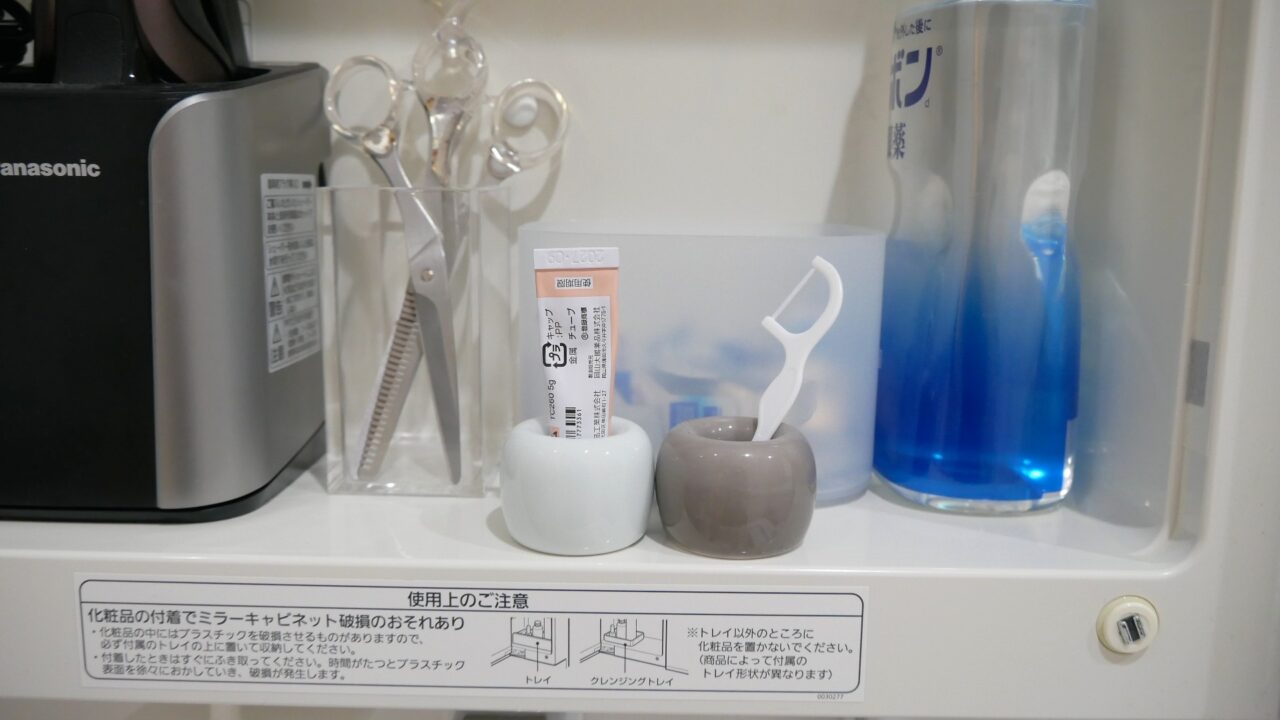 無印良品の歯ブラシスタンドに、小さい薬のチューブと歯間フロスを立てている様子。
