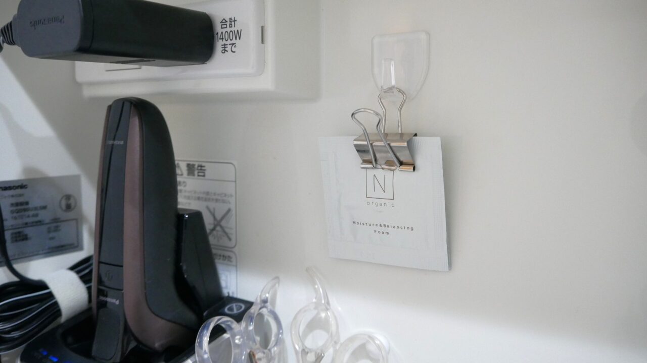 使いかけの化粧品パウチパックをクリップで挟み、鏡裏収納の壁面に取り付けたフックにかけている様子。