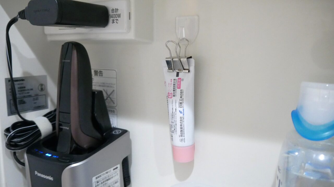 大きめの薬チューブをクリップで挟み、鏡裏収納の壁面に取り付けたフックにひっかけている様子。