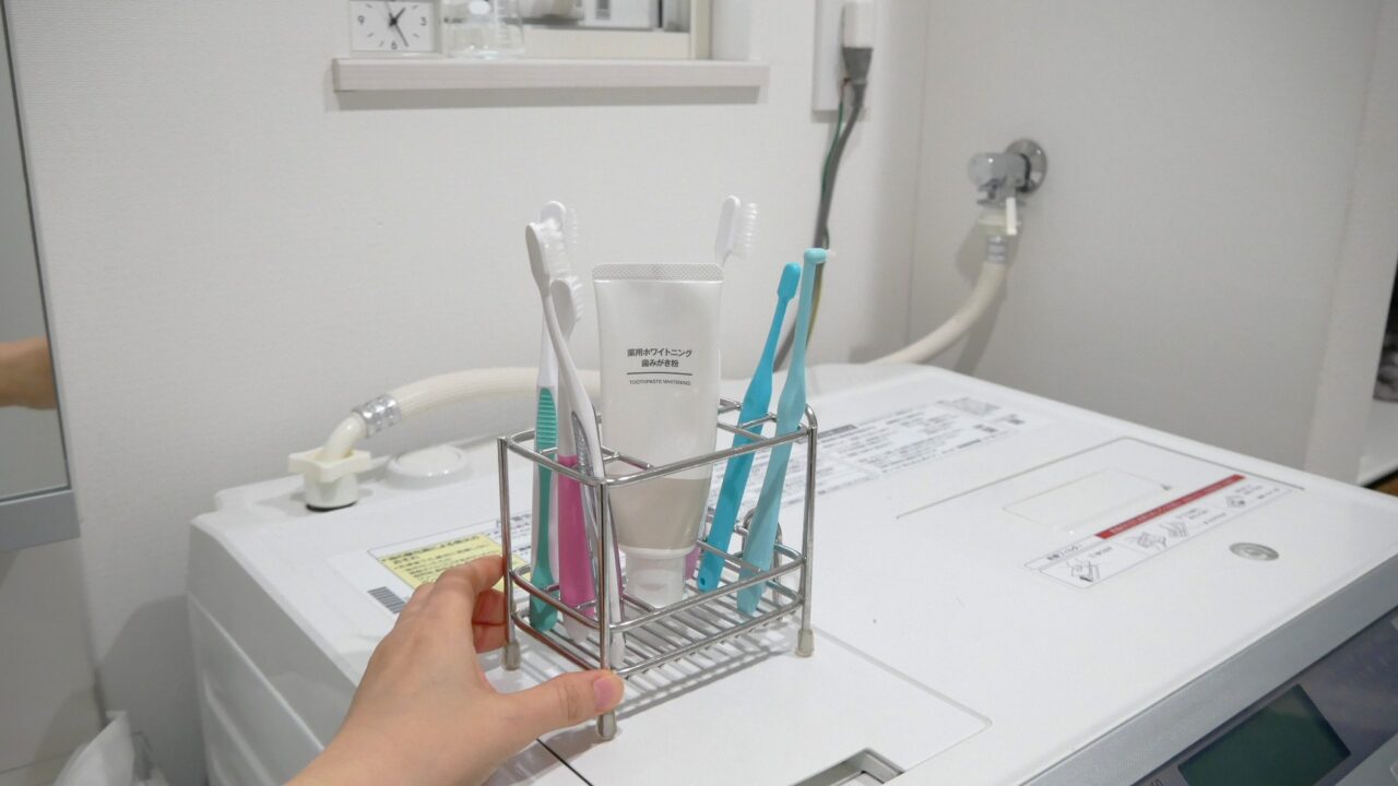 複数の歯ブラシが入ったスタンドを手で持ち、洗濯機の上に移動させている様子。